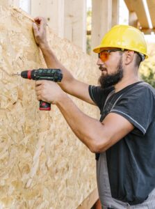 side view construction worker drilling plywood